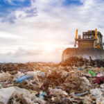 bulldozer working on landfill with birds in the sky.